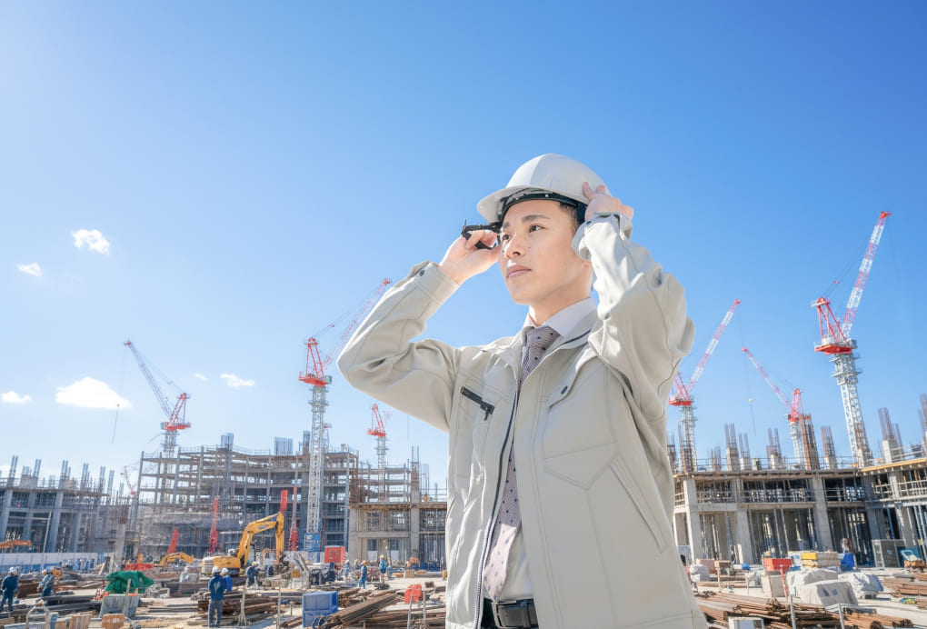 白いヘルメットを着用した担当者が建設現場で機器を調整している写真